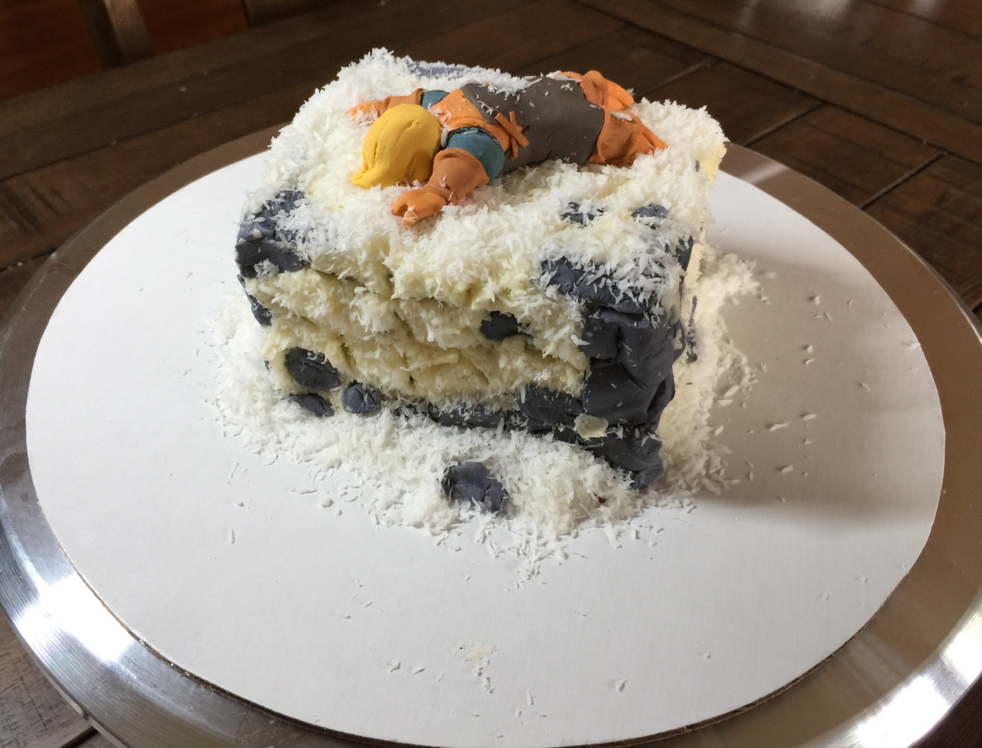 A small cake depicting a gumpaste Algus face down in a pile of coconut snow